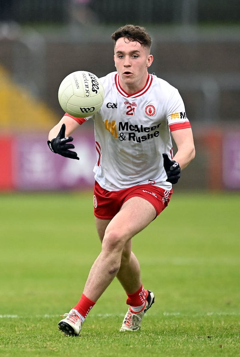 A man in a White Tyrone jersey and red Tyrone gaa shorts catching a ball