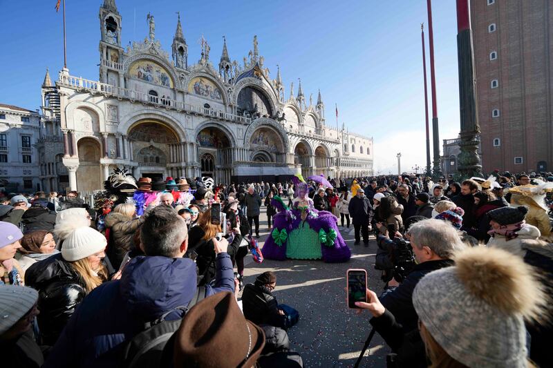 A woman wearing a mask poses in front of St Mark’s church during the Venice Carnival (AP Photo/Luca Bruno)