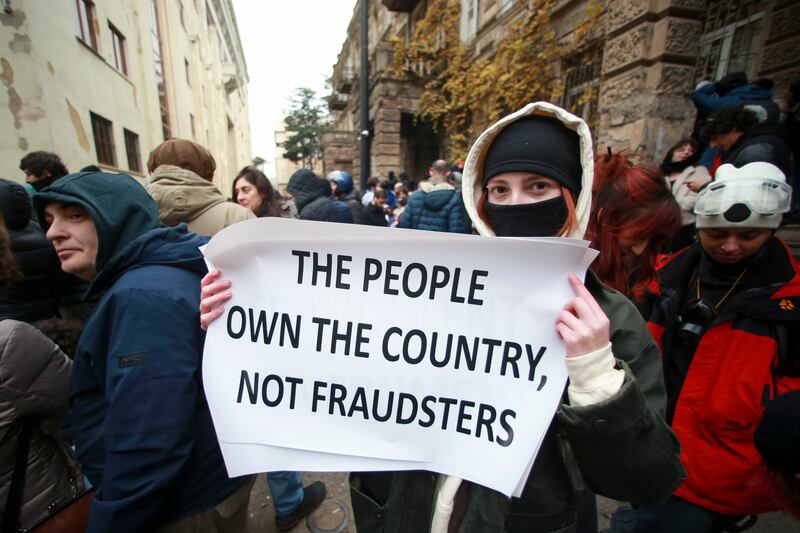 A protester holds a poster during a rally to demand new parliamentary elections in the country, near the parliament’s building in Tbilisi (Zurab Tsertsvadze/AP)