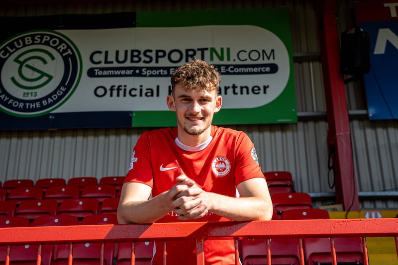 A man smiling in a football stand wearing a Larne FC leaning over a red bar