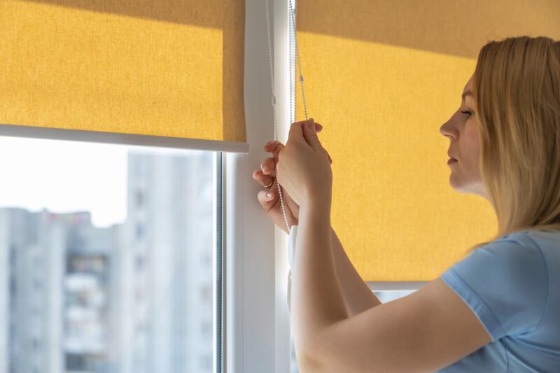 Woman closing yellow blinds