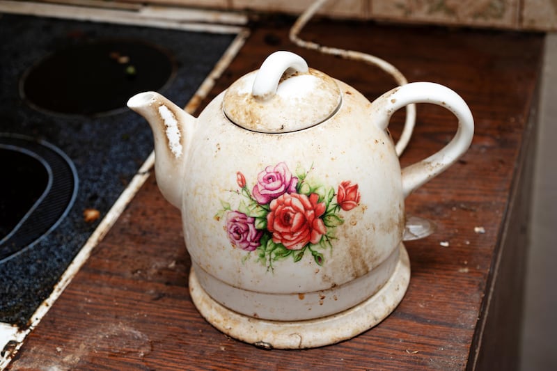 A dirty electric kettle that has a pink flower pattern on it