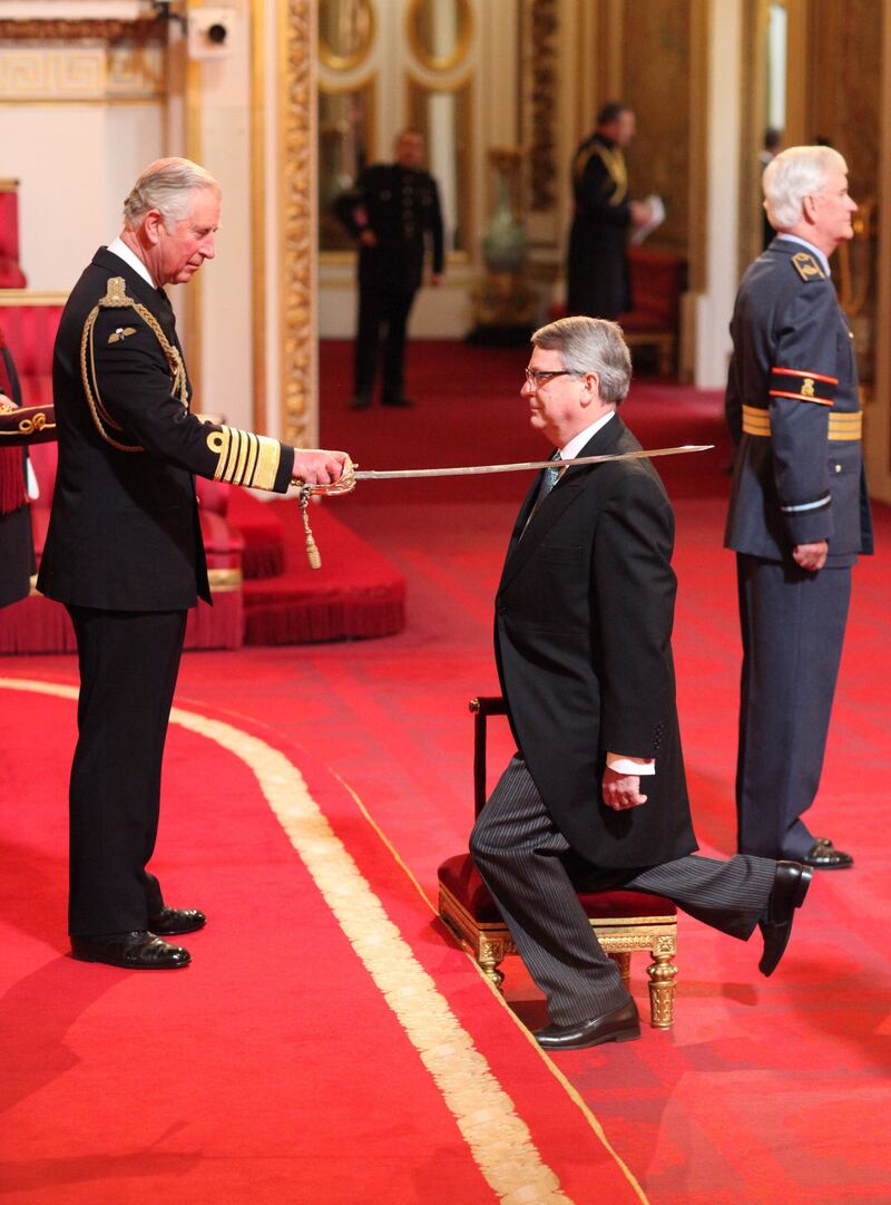 Lynton Crosby, who acted as David Cameron's general election campaign director, is knighted by the Prince of Wales with a sword on his shoulder during a ceremony on a red carpet at Buckingham Palace