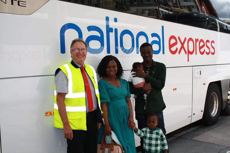 Family of four with coach driver stood beside National Express coach