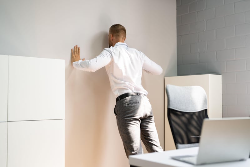 Man wearing a white shirt and grey suit trousers doing a push up against a wall