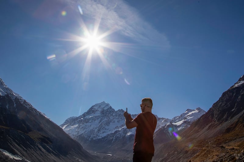 A tourist takes a photo at a frozen lake at the foot of New Zealand’s highest peak, Aoraki, in the Aoraki/Mount Cook National Park (Mark Baker/AP)