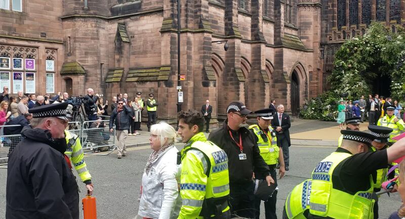 A woman is led away by police after protesters used a fire extinguisher to project orange powder outside Chester Cathedral during the wedding