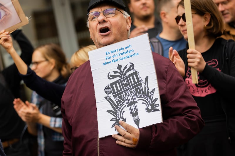 A participant in a protest organised by the Citizens’ Initiative for a Potsdam without a Garrison Church holds a sign at the opening of the church’s tower in Potsdam (Christoph Soeder/AP)