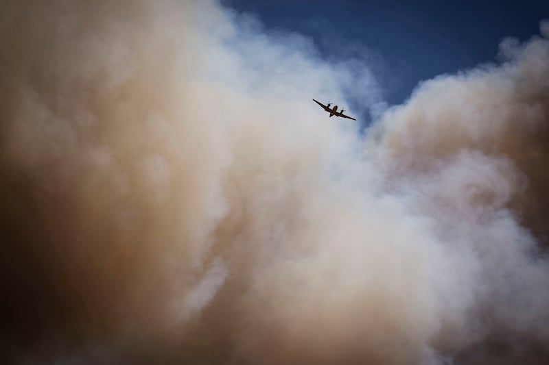 An air tanker soars through a large plume of smoke over and around wildfire-affected areas in the village of Ruidoso, New Mexico (Chancey Bush/The Albuquerque Journal via AP)