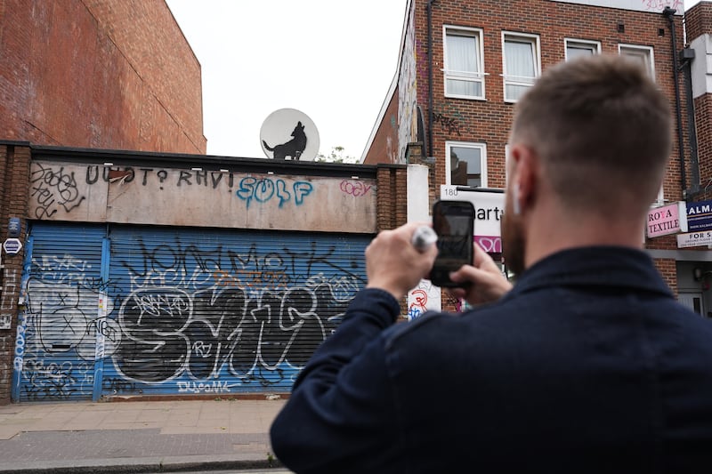 A man takes a picture of the new howling wolf Banksy in Peckham, south London