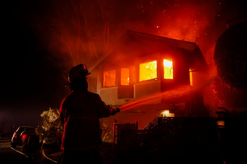 A firefighter works as the Palisades fire burns a house