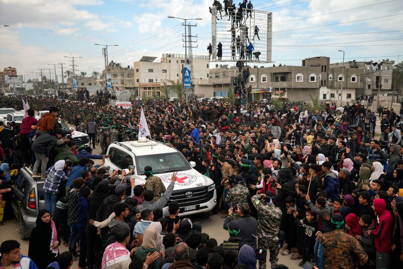 Palestinians gather as Hamas fighters escort Red Cross vehicles carrying the captives in Deir al-Balah, central Gaza Strip (Abdel Kareem Hana/AP)