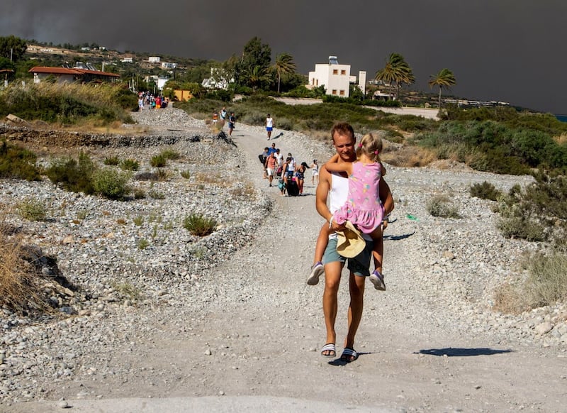 A man carries a child as they leave an area where a forest fire burns on the island of Rhodes. Picture by Lefteris Diamanidis/InTime News via AP
