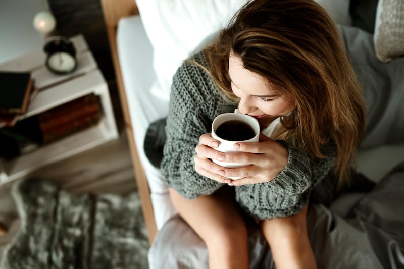 Brunette woman drinking a cup of coffee in bed