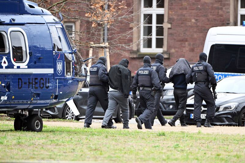 Two people are led from a helicopter to a car by police officers at a helipad in Karlsruhe, Germany, on Friday (Uli Deck/dpa via AP)