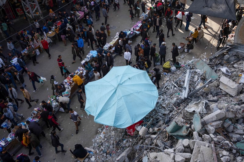 Palestinians buy food at a local market next to a destroyed residential building (Fatima Shbair/AP)