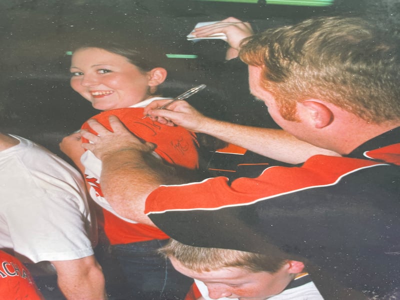 Armagh fan Grainne Loughran smiling at the camera whilst Armagh goalkeeper Bernei Tierney signs the back of her Armagh jersey