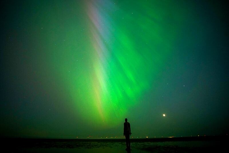 The aurora borealis, also known as the northern lights, glow on the horizon at Another Place by Anthony Gormley, Crosby Beach, Liverpool