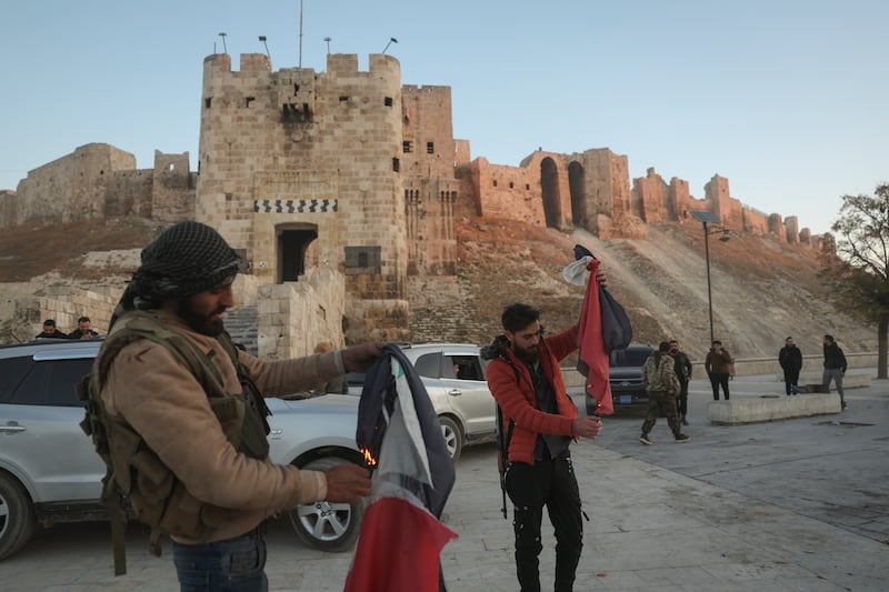 Syrian opposition fighters burn government Syrian flags for the cameras next to Aleppo’s old city (Ghaith Alsayed/AP)