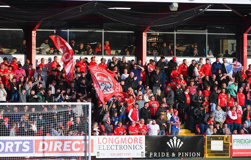 A football stand at Inver Park full of fans and flags of Larne Football Club