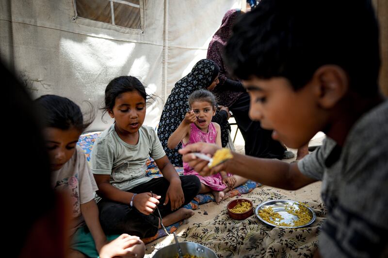 Members of the Al-Ashqar family, who were displaced by the Israeli bombardment of the Gaza Strip, eat lunch at a makeshift tent camp in Khan Younis (Abdel Kareem Hana/AP)
