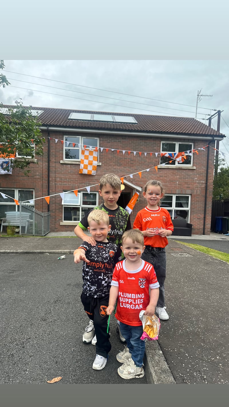 Children standing outside a house dressed in Armagh jerseys and Clann Eireann jerseys, with bunting and flags on the house behind them