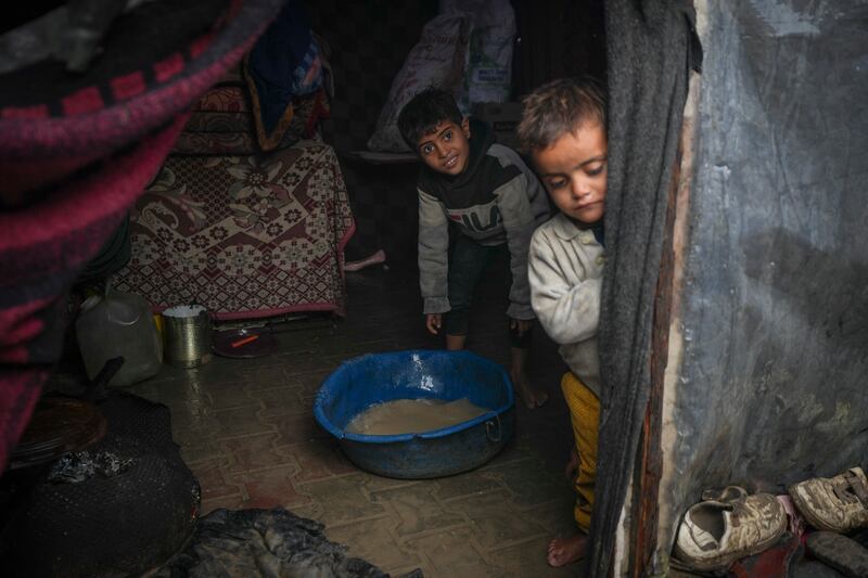 Two young Palestinian brothers help clear water from their flooded family tent after overnight rain at the refugee camp in Deir al-Balah, central Gaza Strip (Abdel Kareem Hana/AP)