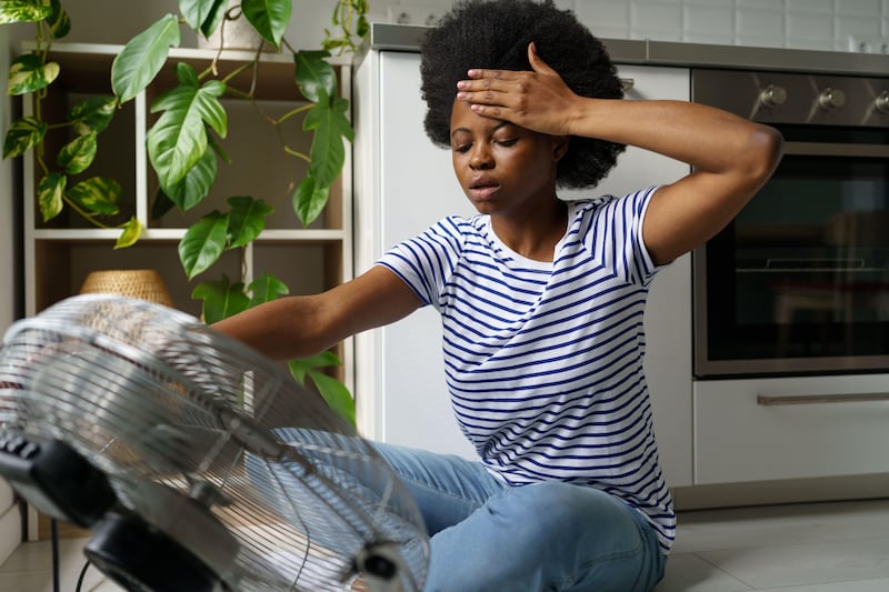 Exhausted young woman sat in front of a fan experiencing hot flashes