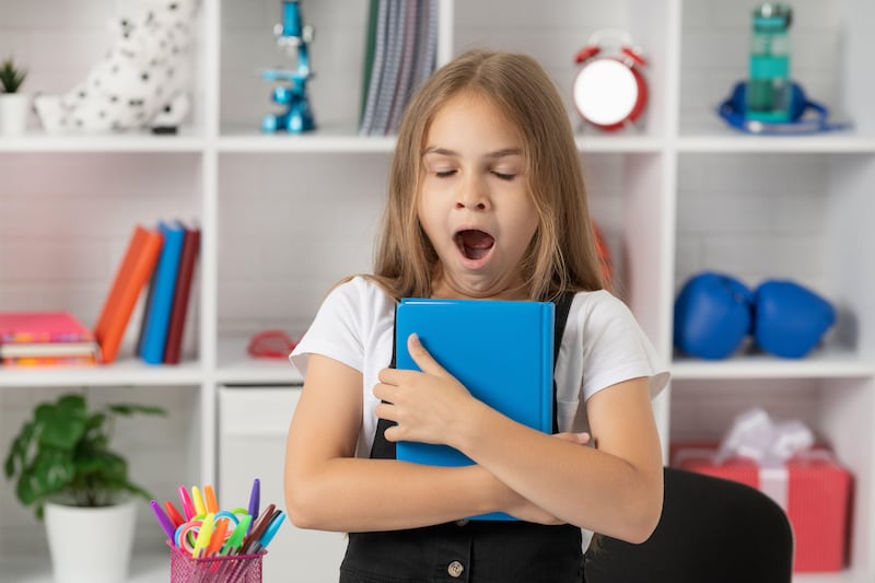 Young girl yawning in class while holding a notebook