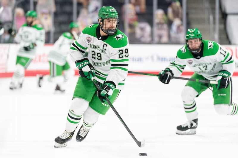 Jordan Kawaguchi in a white and green University of North Dakota dribbling a puck