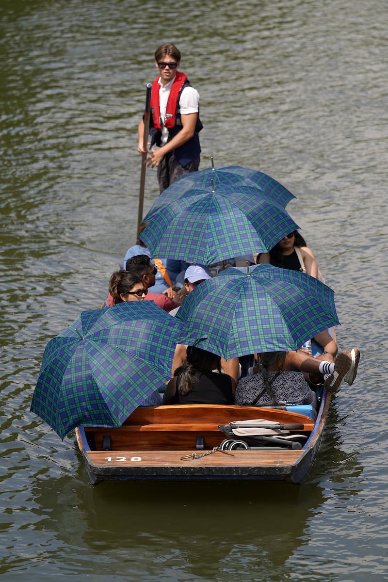 People shelter from the sun under umbrellas as they take a punt tour along the River Cam in Cambridge