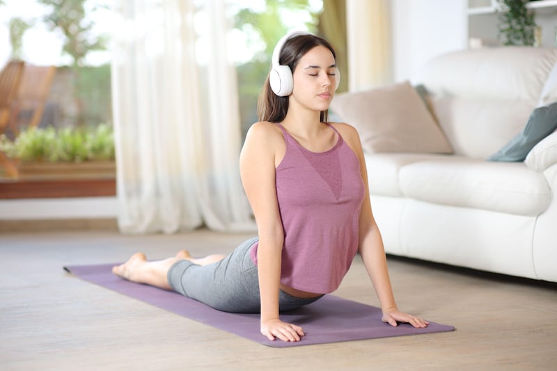 Teenage girl wearing headphones and doing yoga exercises at home