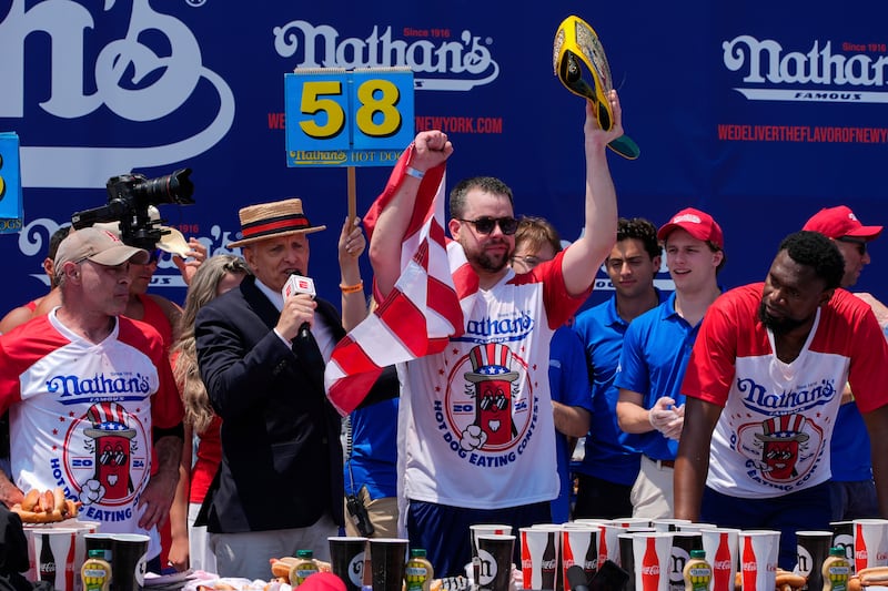 Patrick Bertoletti, centre, reacts after winning the men’s division in Nathan’s Famous Fourth of July hot dog eating contest (Julia Nikhinson/AP)