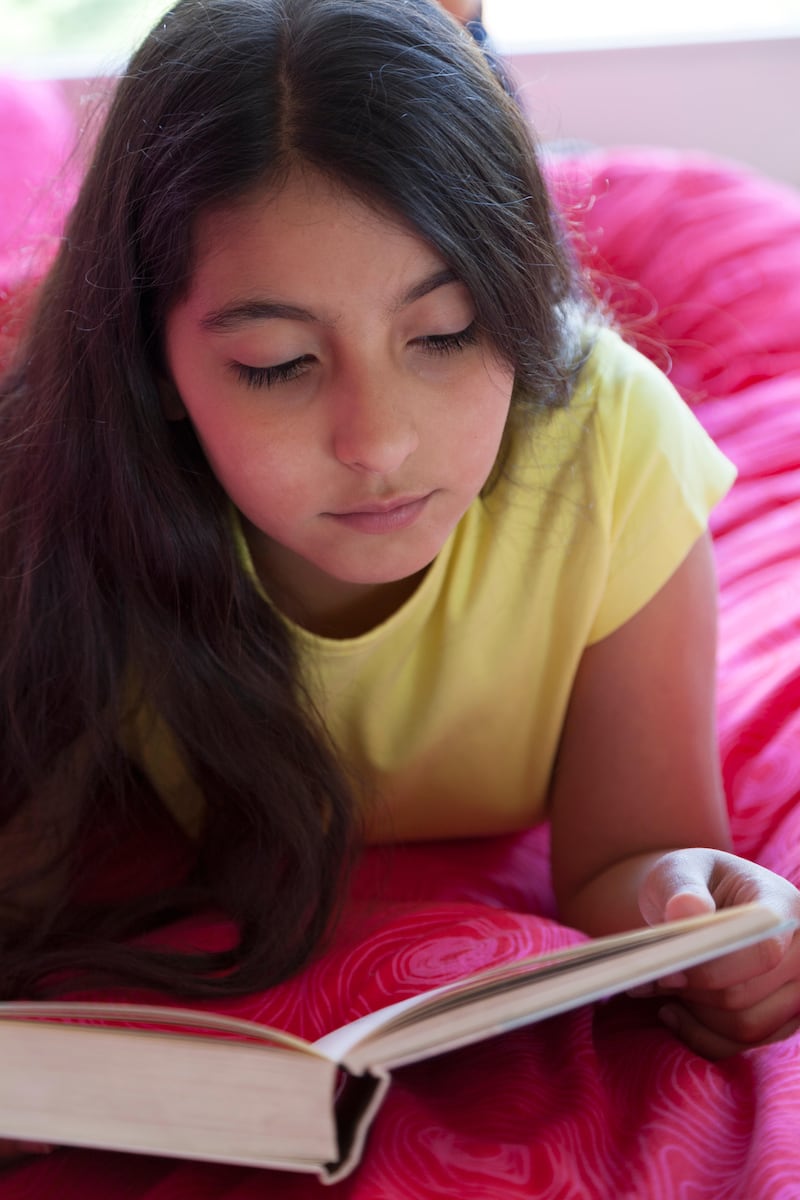 Teenage girl reading a book in bed