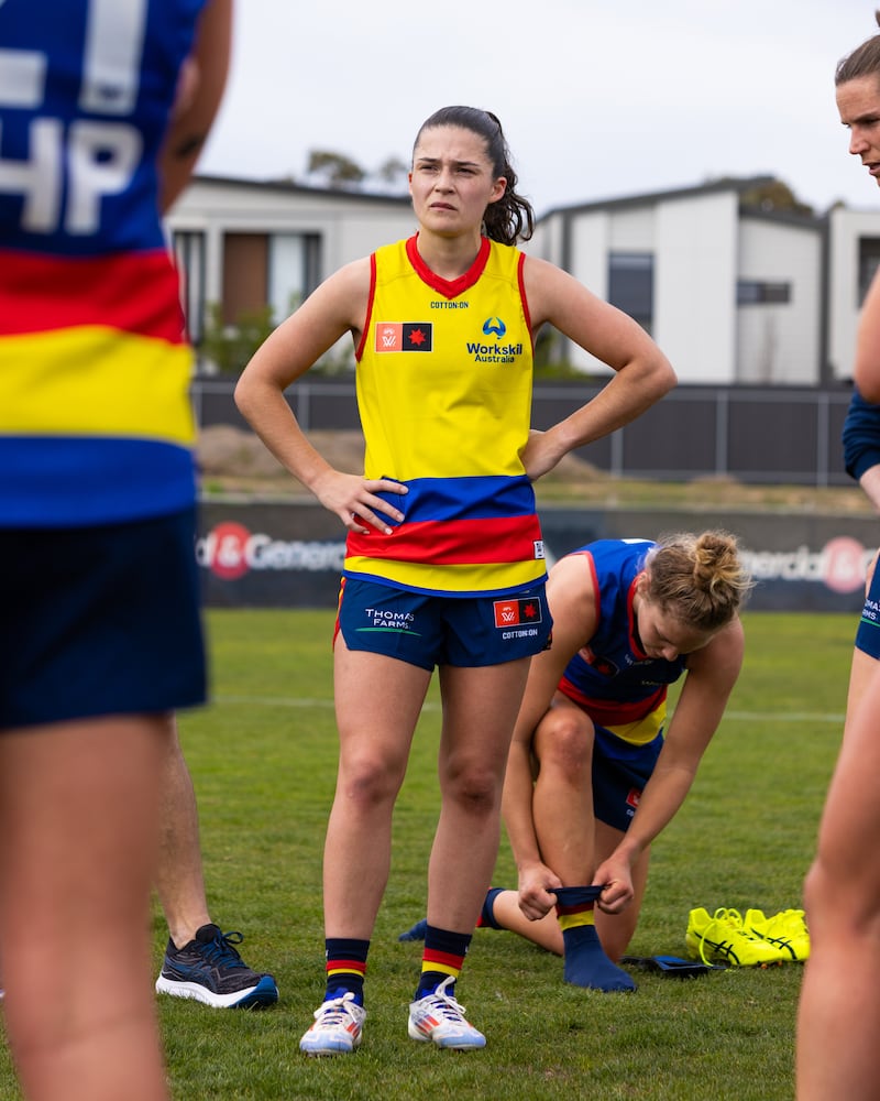 A woman standing with her hands on her hips listening to a coach in a yellow jersey with red and blue stripes