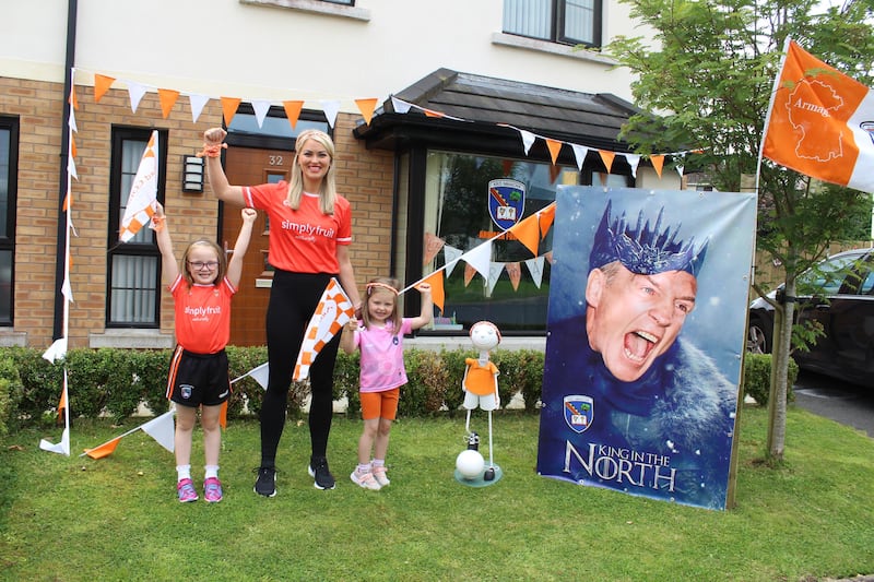 Ciara McGill and children Erin and Ceola McGill standing in their garden surrounded by Armagh decorations, including a poster of Kieran McGeeney dressed as a character from Game of Thrones with the caption 'King in the North;