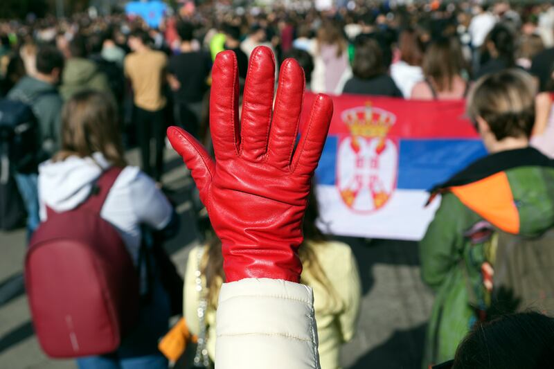 A woman raises a red glove symbolising blood during the student-led 24-hour blockade at an intersection in Belgrade (Darko Vojinovic/AP)