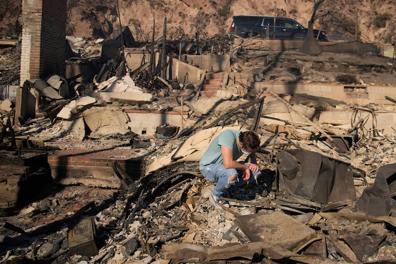 Luke Dexter kneels as he sifts through the remains of his father’s fire-ravaged beach-front property in Malibu (John Locher/AP)