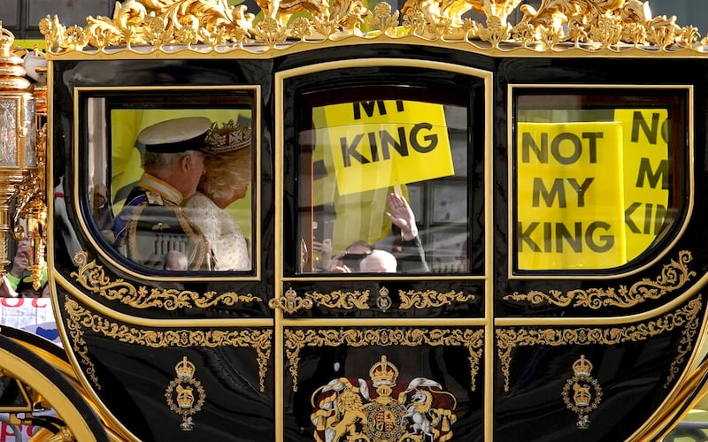 The state coach carrying the King and Queen passes by protesters from anti-monarchy pressure group Republic at the last State Opening of Parliament