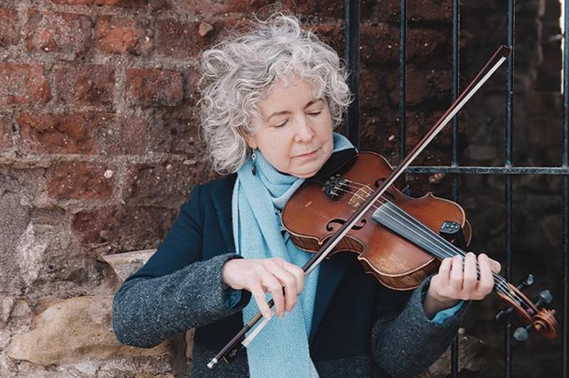 Photo of Bríd Harper playing the fiddle wearing a green scarf with a brick background
