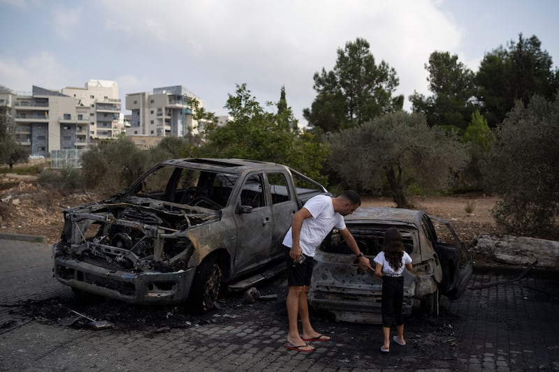 A man shows a girl a burnt-out car after a rocket launched from Lebanon hit an area in Kfar Vradim, northern Israel (Leo Correa/AP)