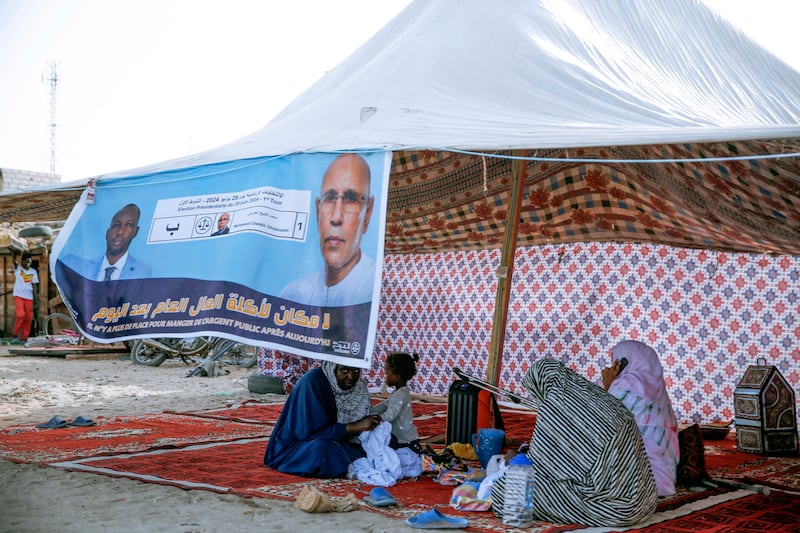 Women sit behind an electoral banner for Mauritanian president Mohamed Ould Ghazouani, during a campaign rally before the presidential elections. The banner reads: “There is no place for people embezzling public funds any more” (Mamsy Elkeihel/AP)