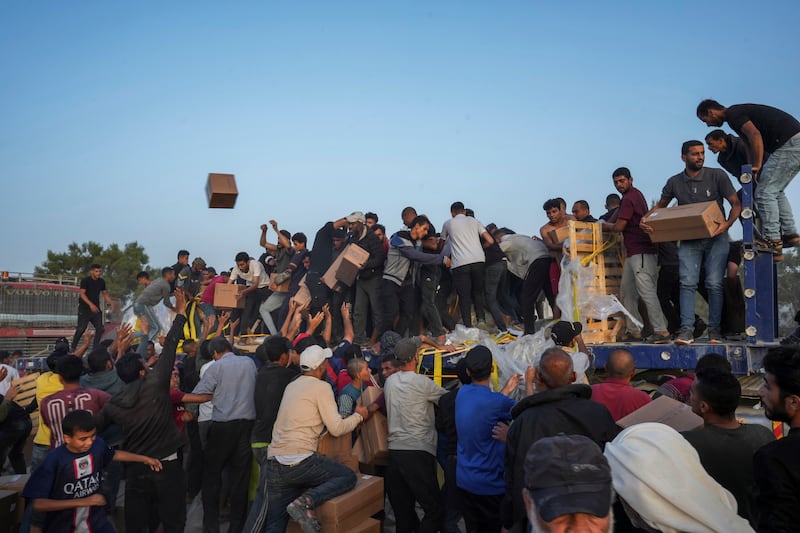 Palestinians storming lorries loaded with humanitarian aid (Abdel Kareem Hana/AP)