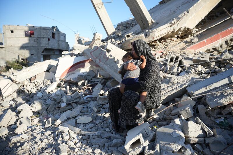 A mother holds her daughter on the remains of a damaged building in Gaza.