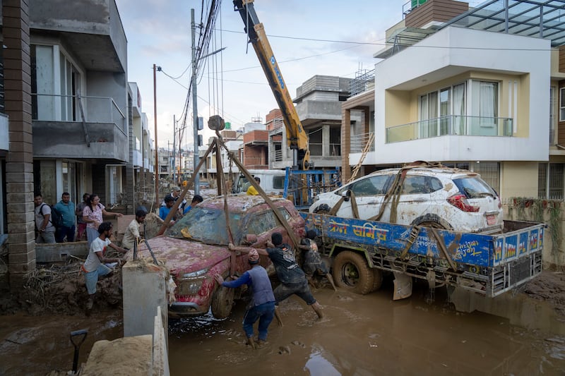 A group of men use a crane to lift vehicles out of the mud after flooding caused by heavy rains in Nepal (Niranjan Shrestha/AP)