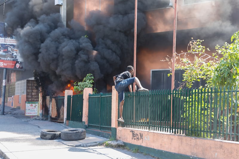 A man climbs into the office of Haiti’s power company, set on fire during protests (Odelyn Joseph/AP)