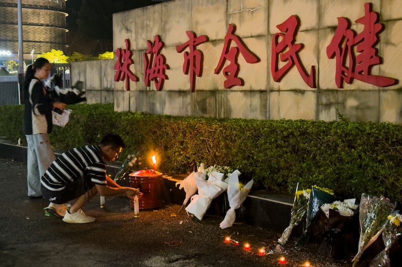 A man lights a candle near flowers placed outside the Zhuhai People’s Fitness Plaza, where a man deliberately rammed his car into people exercising at the sports centre (Ng Han Guan/AP)