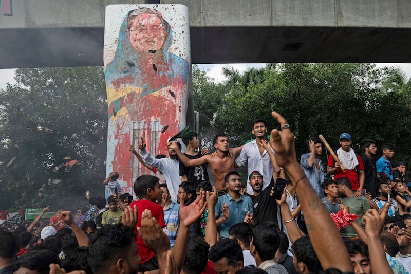 Protesters celebrate beside a defaced portrait of prime minister Sheikh Hasina after news of her resignation, in Dhaka, Bangladesh (Fatima Tuj Johora/AP)