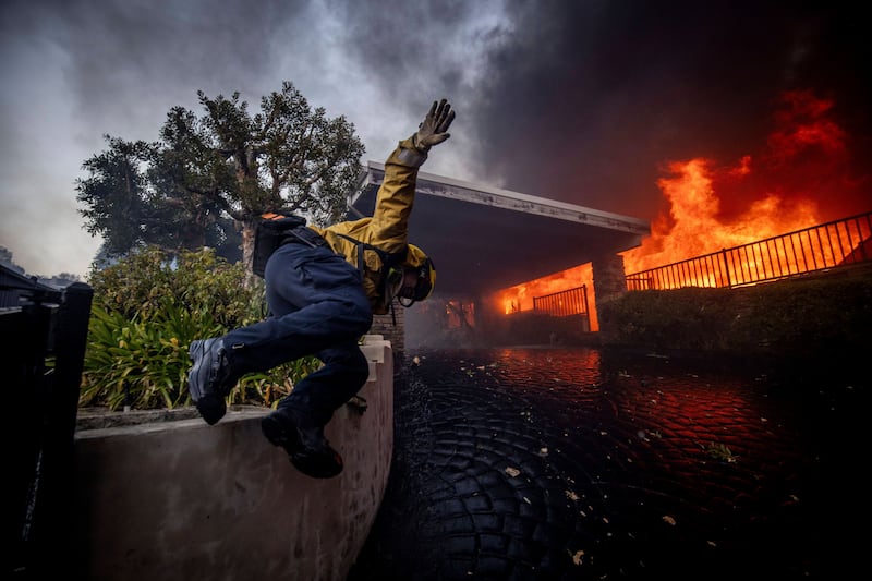 A firefighter jumps over a fence while fighting the Palisades Fire in the Pacific Palisades neighbourhood (Ethan Swope/AP)