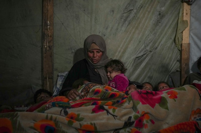 Reda Abu Zarada wraps herself and her grandchildren in blankets as they prepare to sleep in their tent at a camp in Khan Younis, Gaza Strip (Abdel Kareem Hana/AP)